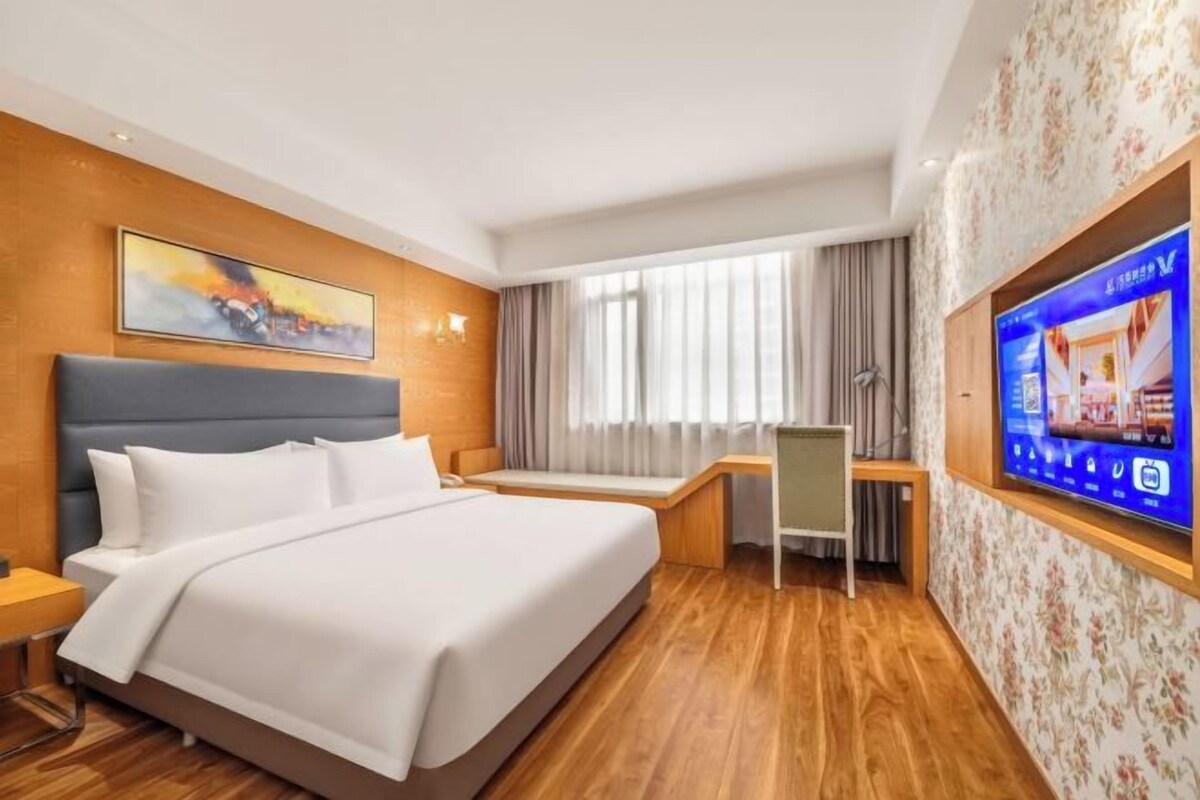 A hotel room with a bed, a desk, a television, and a window with curtains.
