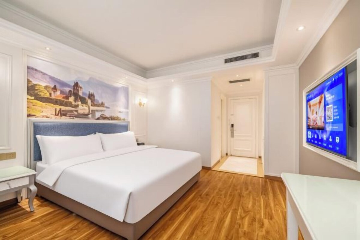 A hotel room with a large bed, a flat-screen TV, and a painting on the wall.
