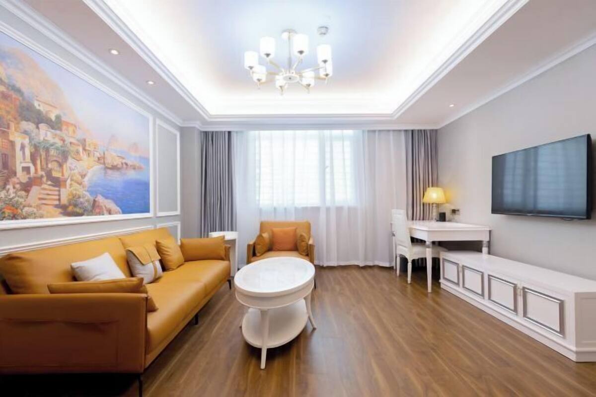 A modern living room with a sofa, a round coffee table, a TV, and a painting on the wall.