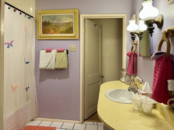 A bathroom with a shower, a sink with a mirror, and a door leading to another room.
