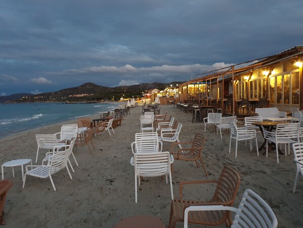 Um restaurante à beira-mar com mesas e cadeiras ao ar livre, com vista para o mar.