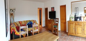 Uma sala de estar com sofá de madeira, TV sobre suporte, mesa de jantar e aparador com objetos decorativos.