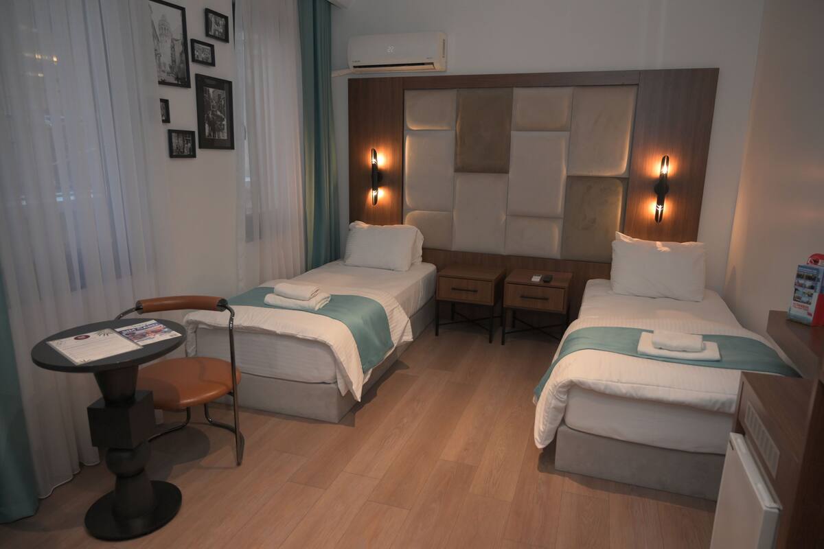 A hotel room with two beds, a desk, a chair, and a table.