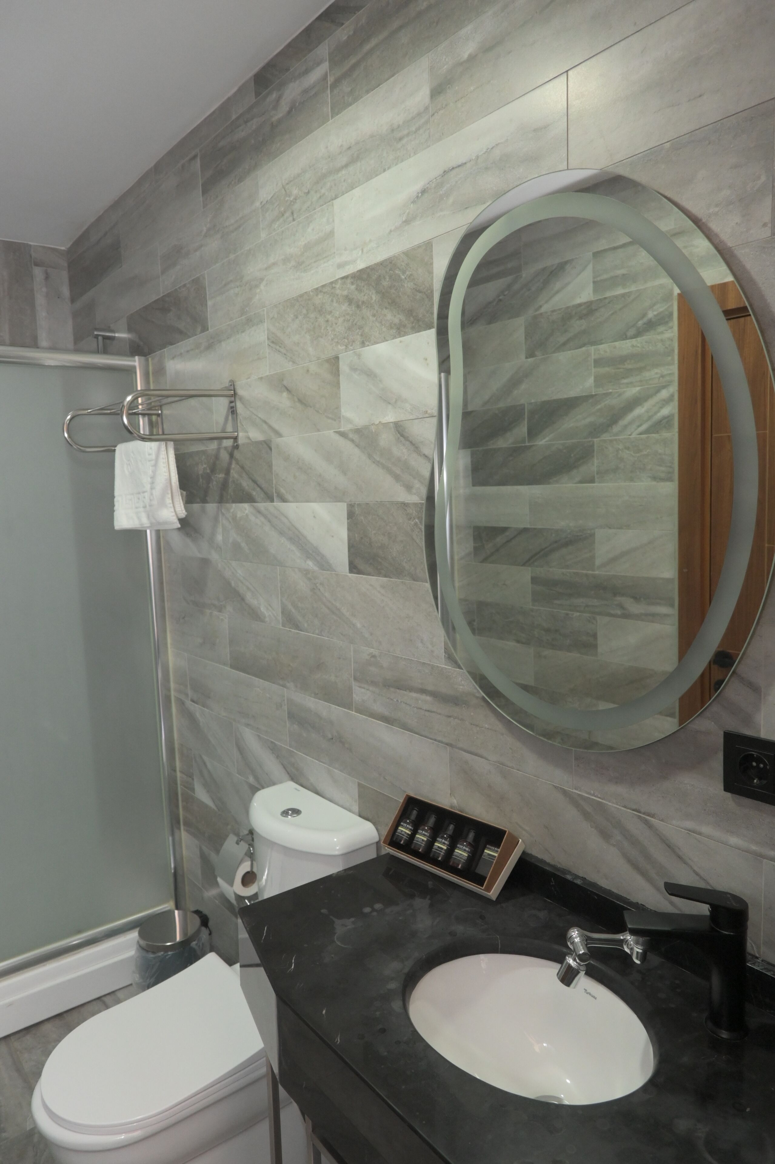 A bathroom with a marble tile wall, a round mirror, a white sink, and a toilet.