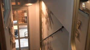 Un escalier recouvert d’une moquette rouge, un mur orné d’une œuvre d’art représentant des palmiers, et une porte donnant sur une pièce avec vue.