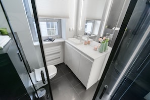 Features a sleek vanity with a large mirror and a window offering a view of the outdoors.
