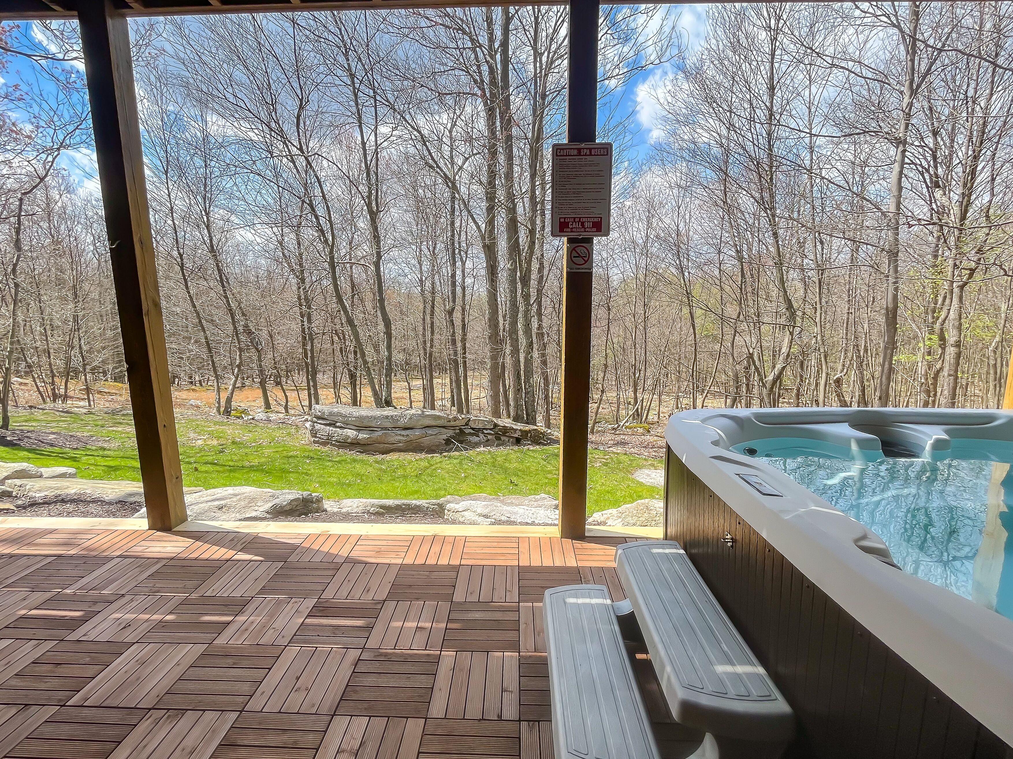 A wooden deck with a hot tub and benches, overlooking a forested area.