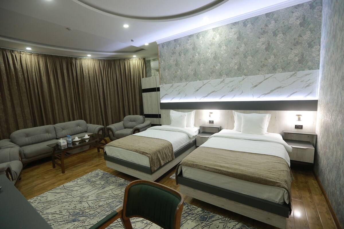 A hotel room with two beds, a sofa, a chair, a coffee table, and a large mirror.