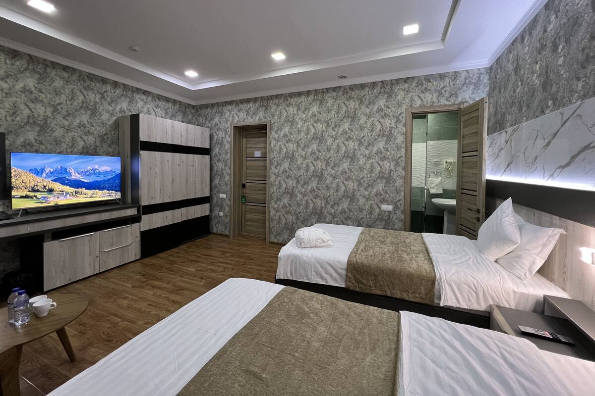 A hotel room with two beds, a TV, a wardrobe, and a bathroom visible through an open door.