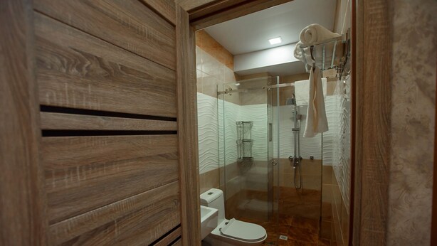A modern bathroom with a wooden vanity, a glass shower enclosure, and a white toilet. - Ada Hotel (Tashkent)