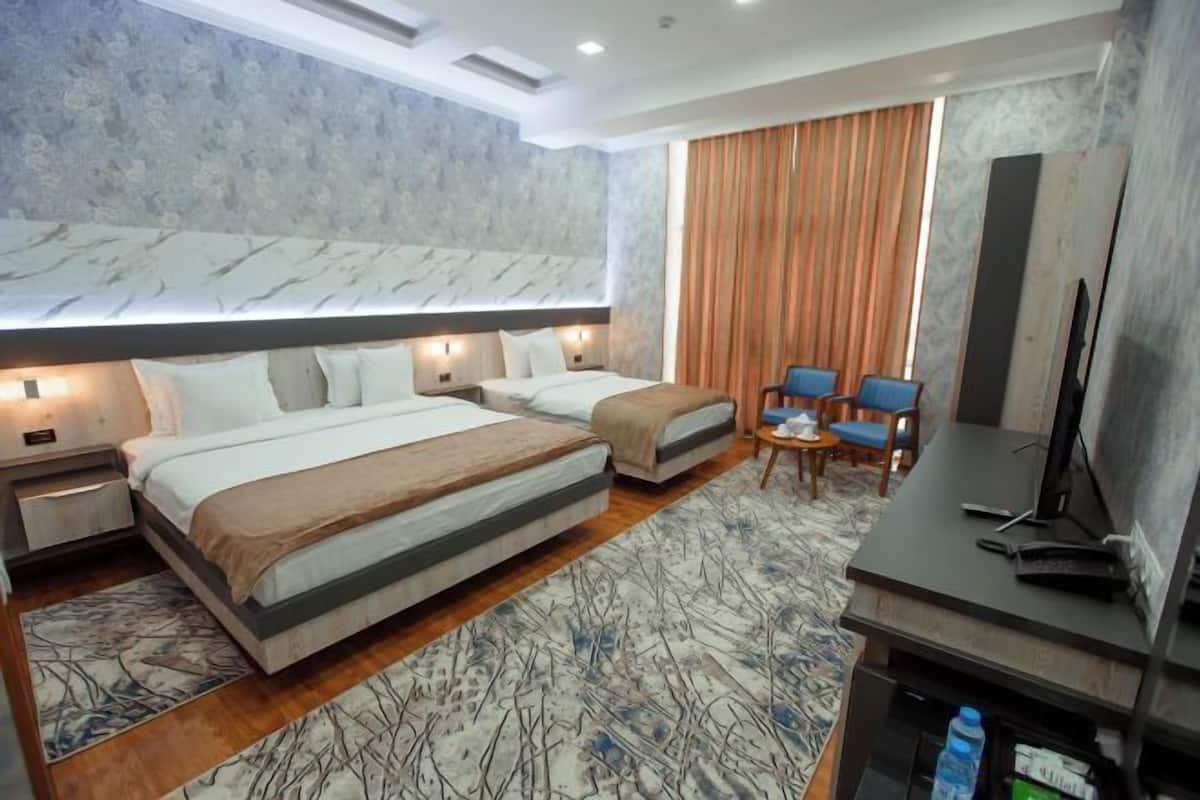 A hotel room with two beds, a desk with a computer, a TV, and a seating area with chairs.