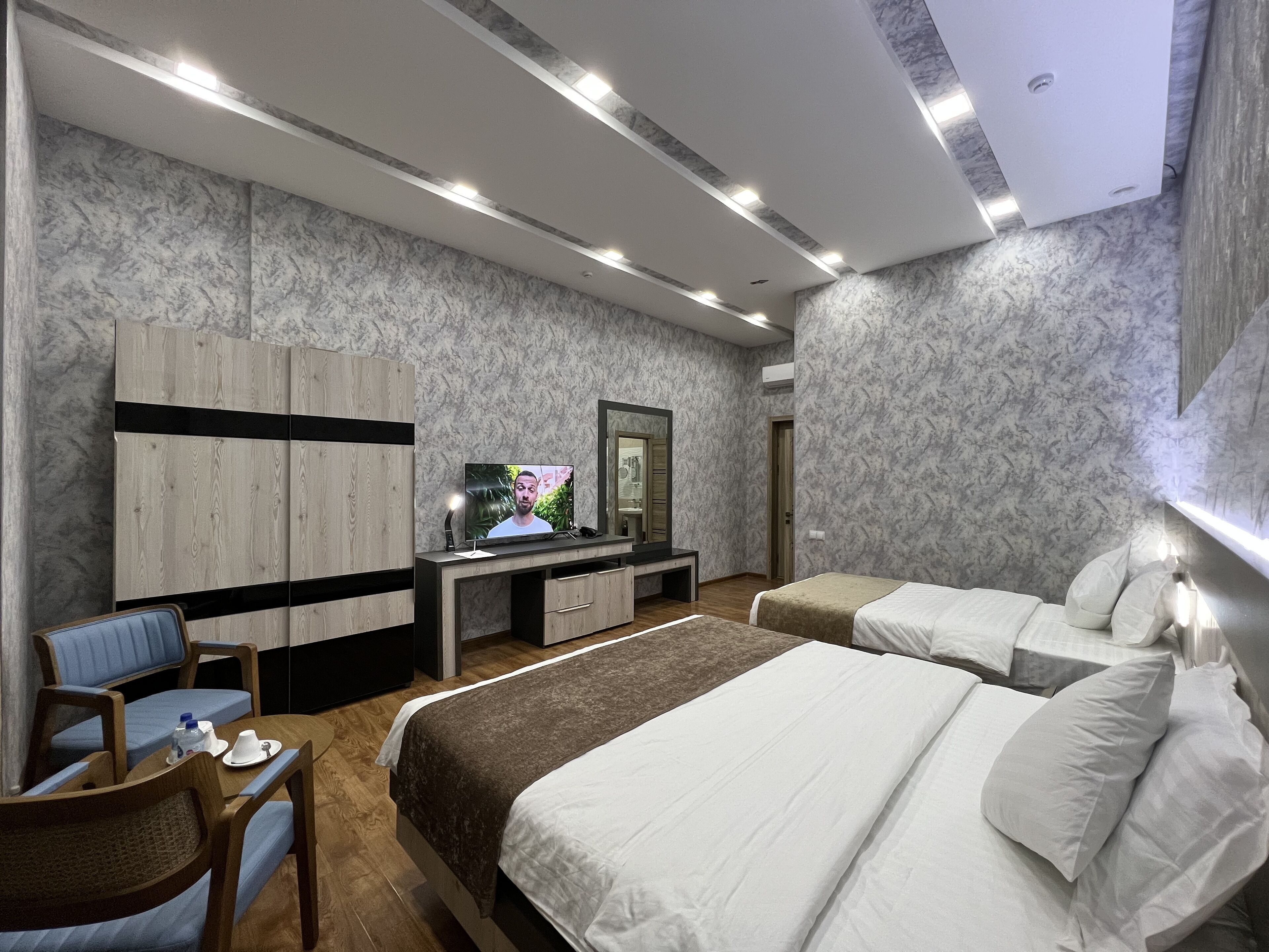 Una camera d'albergo moderna con un letto grande, una scrivania con televisore, un angolo salotto e un bagno.