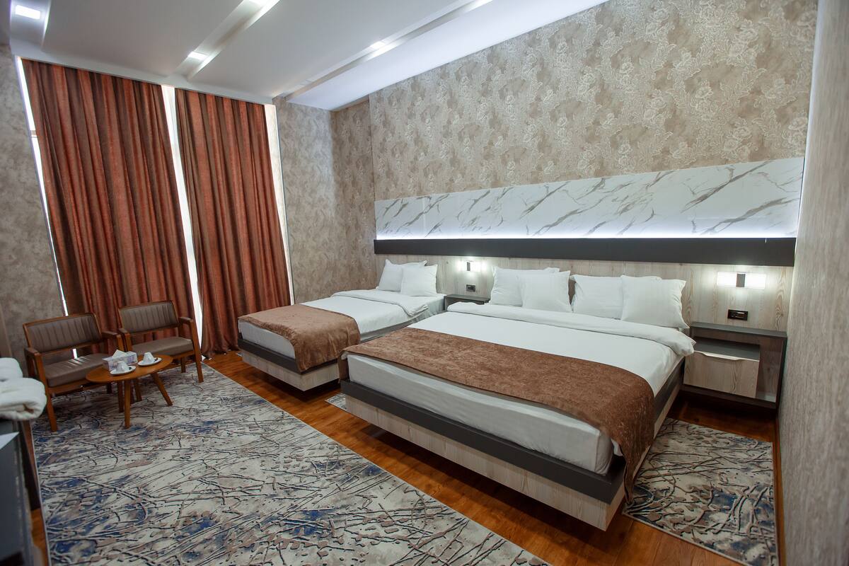 A hotel room with two beds, a sitting area with chairs, a small table, and a large window with curtains.