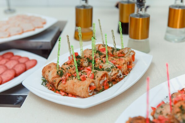 Una mesa de buffet con diversos platos, entre ellos aperitivos enrollados adornados con hierbas y brochetas.