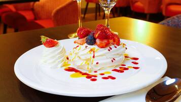 A dessert plate with whipped cream, strawberries, and blueberries, accompanied by a spoon and two glasses of white wine on a table.