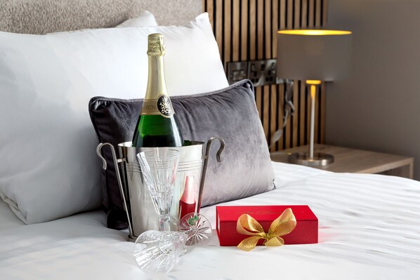 Una cama con una botella de champán, copas y una caja de regalo.
