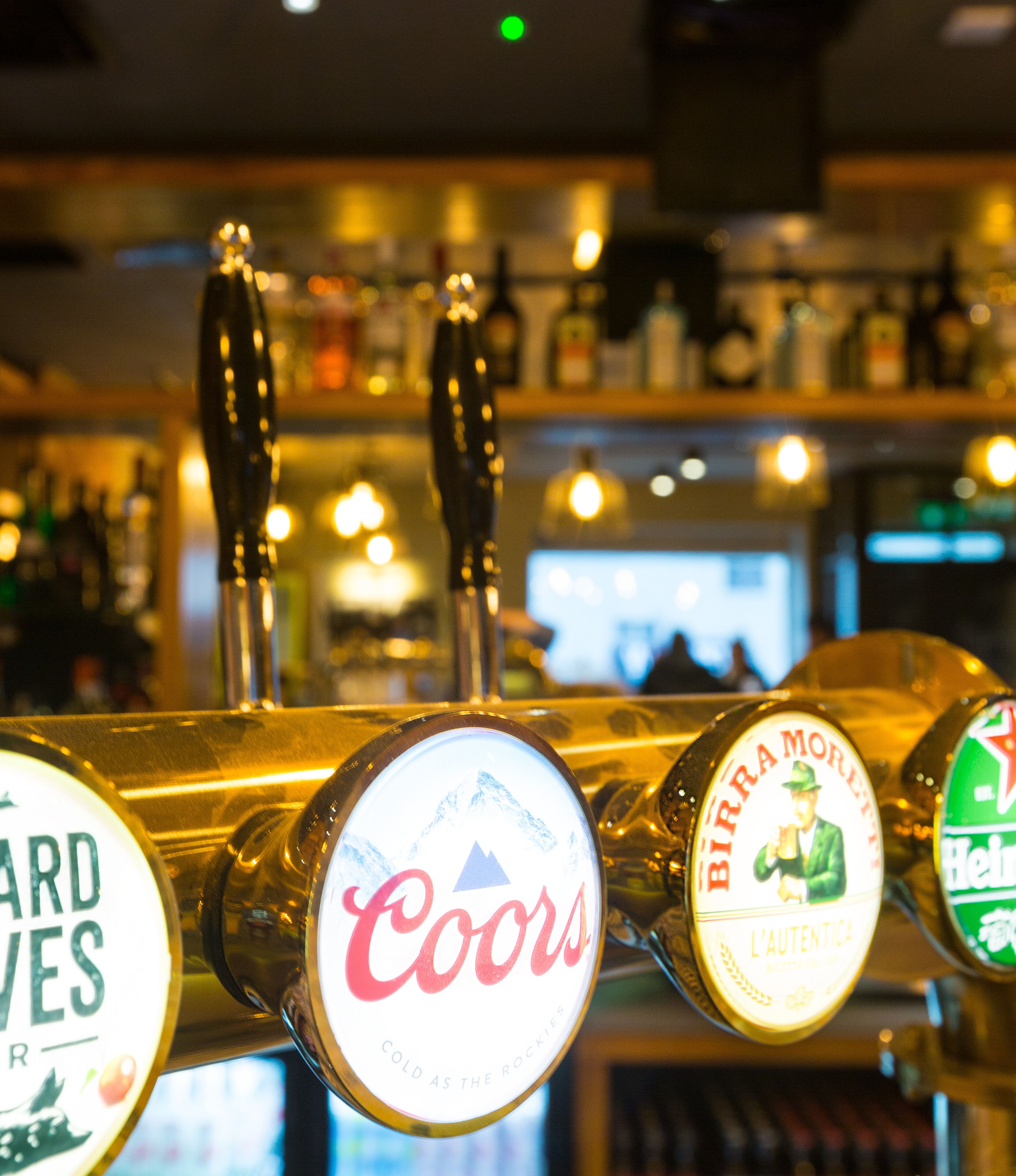 Un bar con múltiples grifos de cerveza, incluyendo marcas como Coors y Heineken.