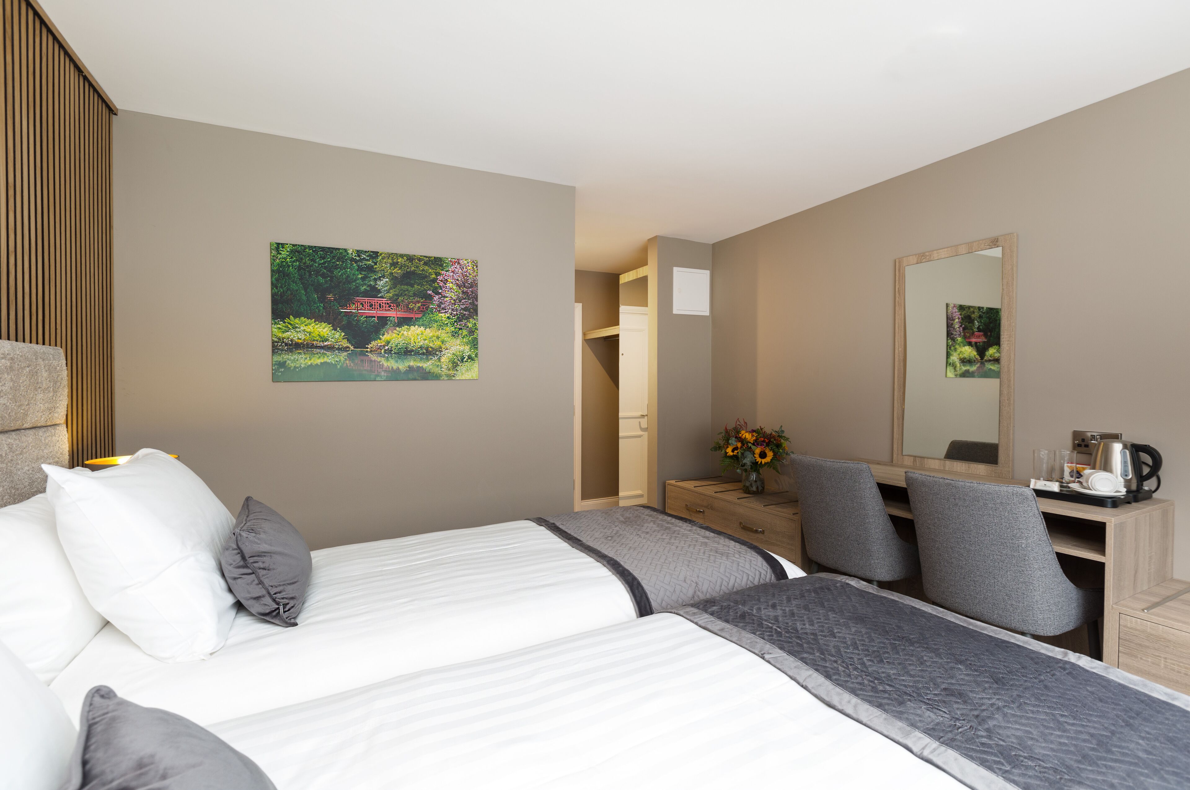 A hotel room with a bed, bedside table, dresser, and a mirror.