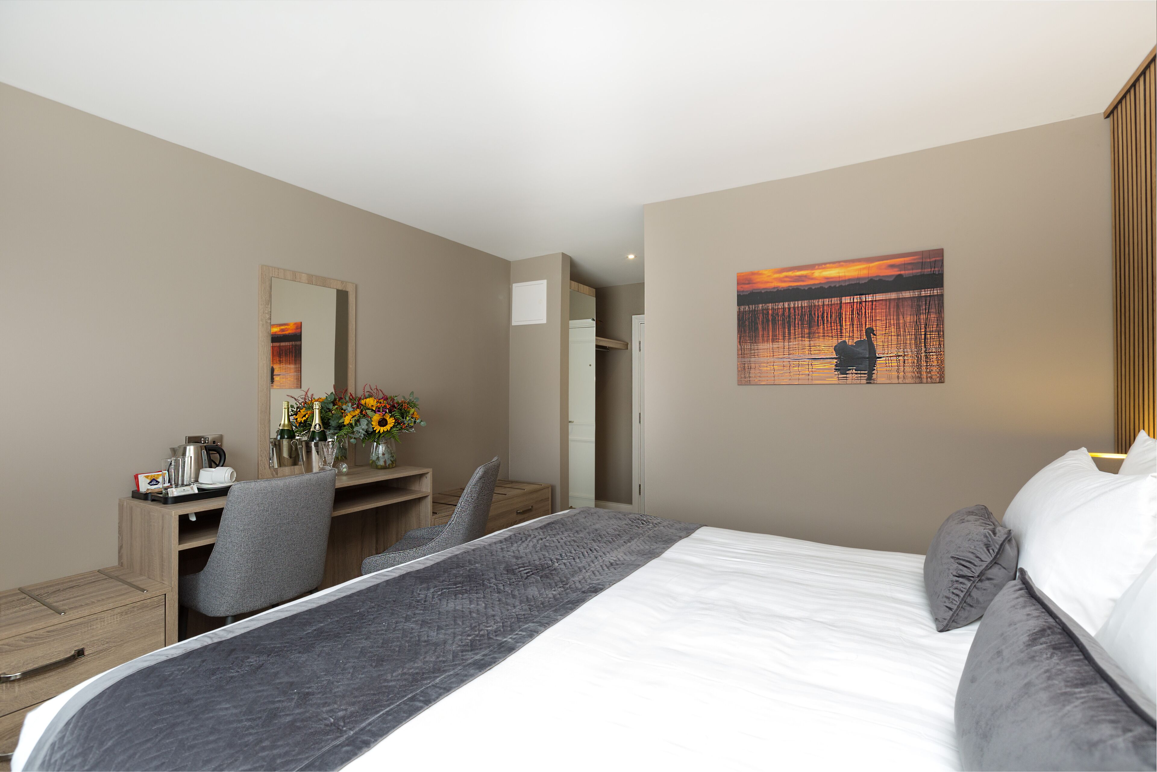 A hotel room with a bed, a desk, a chair, a mirror, and a painting on the wall.