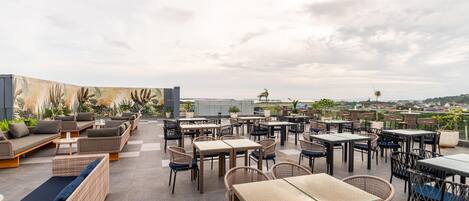 An outdoor patio area with wicker furniture, tables, and chairs, featuring a view of the cityscape.