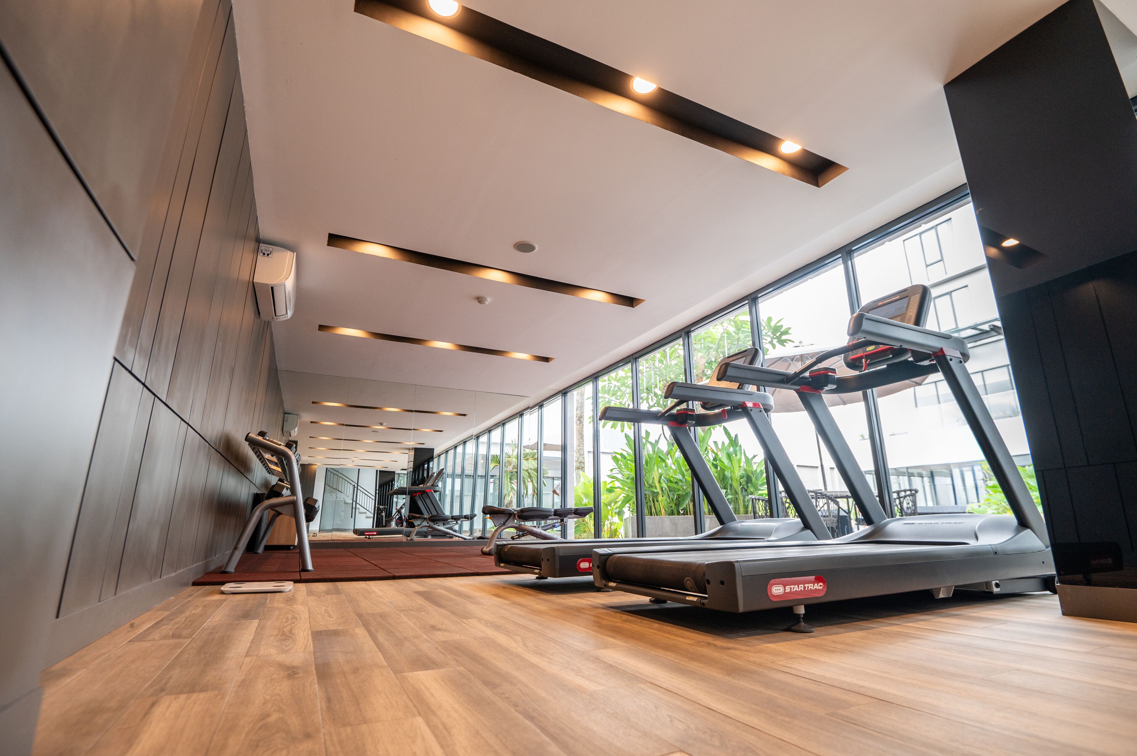 Une salle de sport moderne équipée de tapis de course, d’appareils d’exercice et de grandes fenêtres donnant sur l’extérieur.