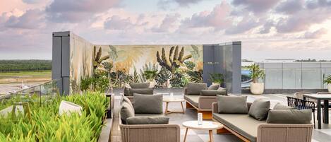 A rooftop lounge with outdoor seating, a mural, and a view of the landscape.