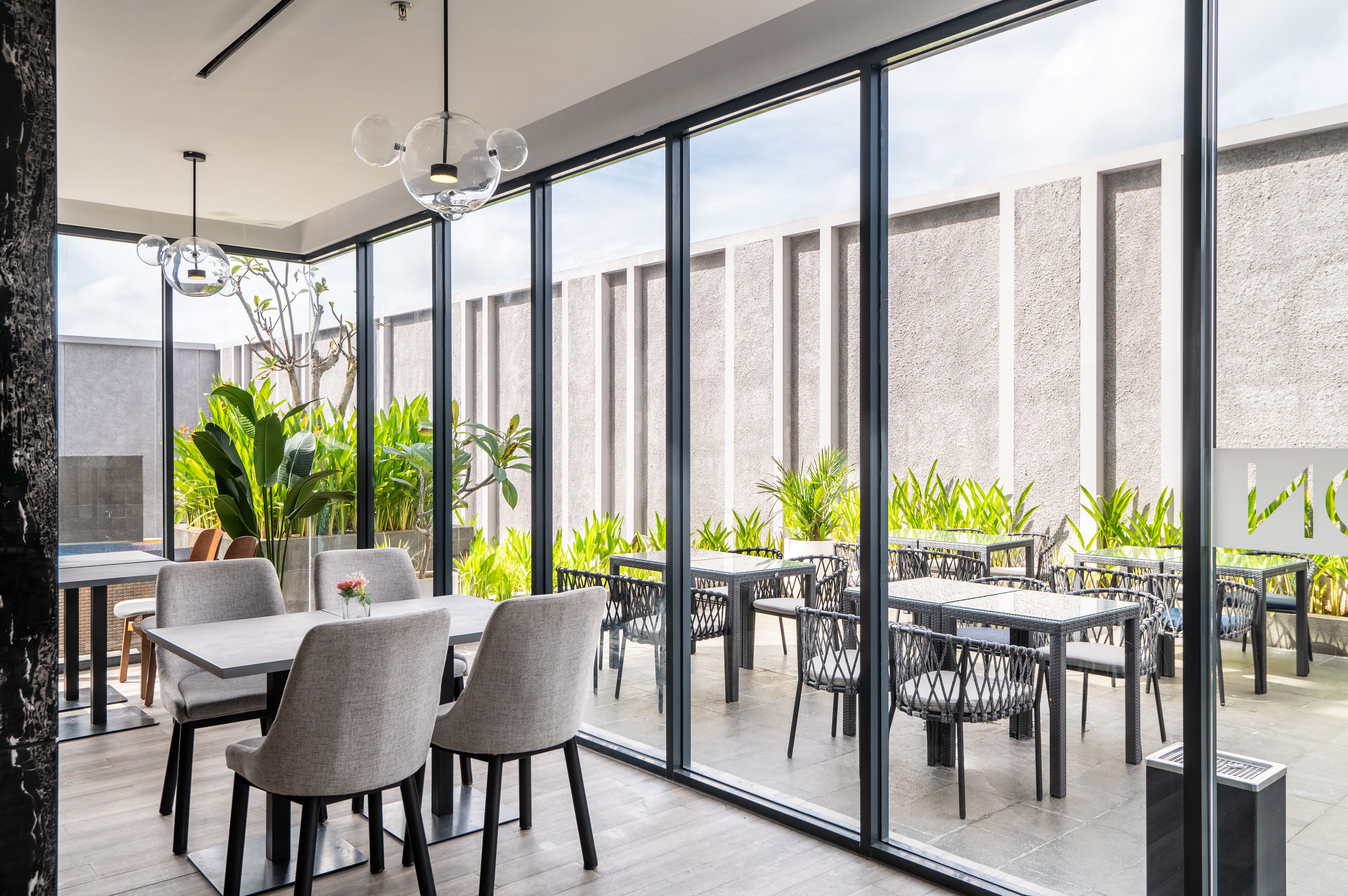 A modern outdoor dining area with glass walls, wicker furniture, and potted plants.