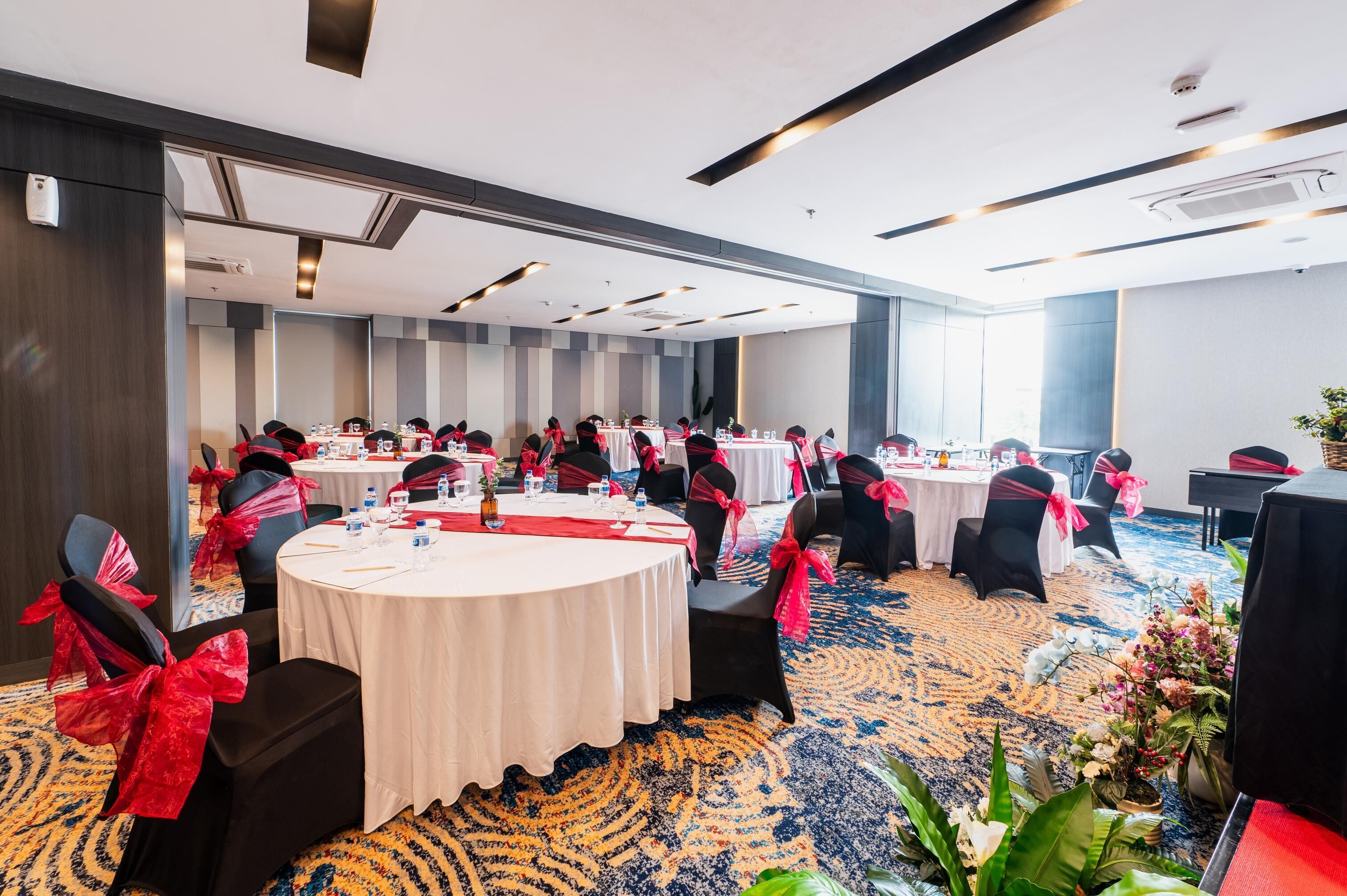 A conference room with round tables, black chairs with red sashes, and a carpeted floor.