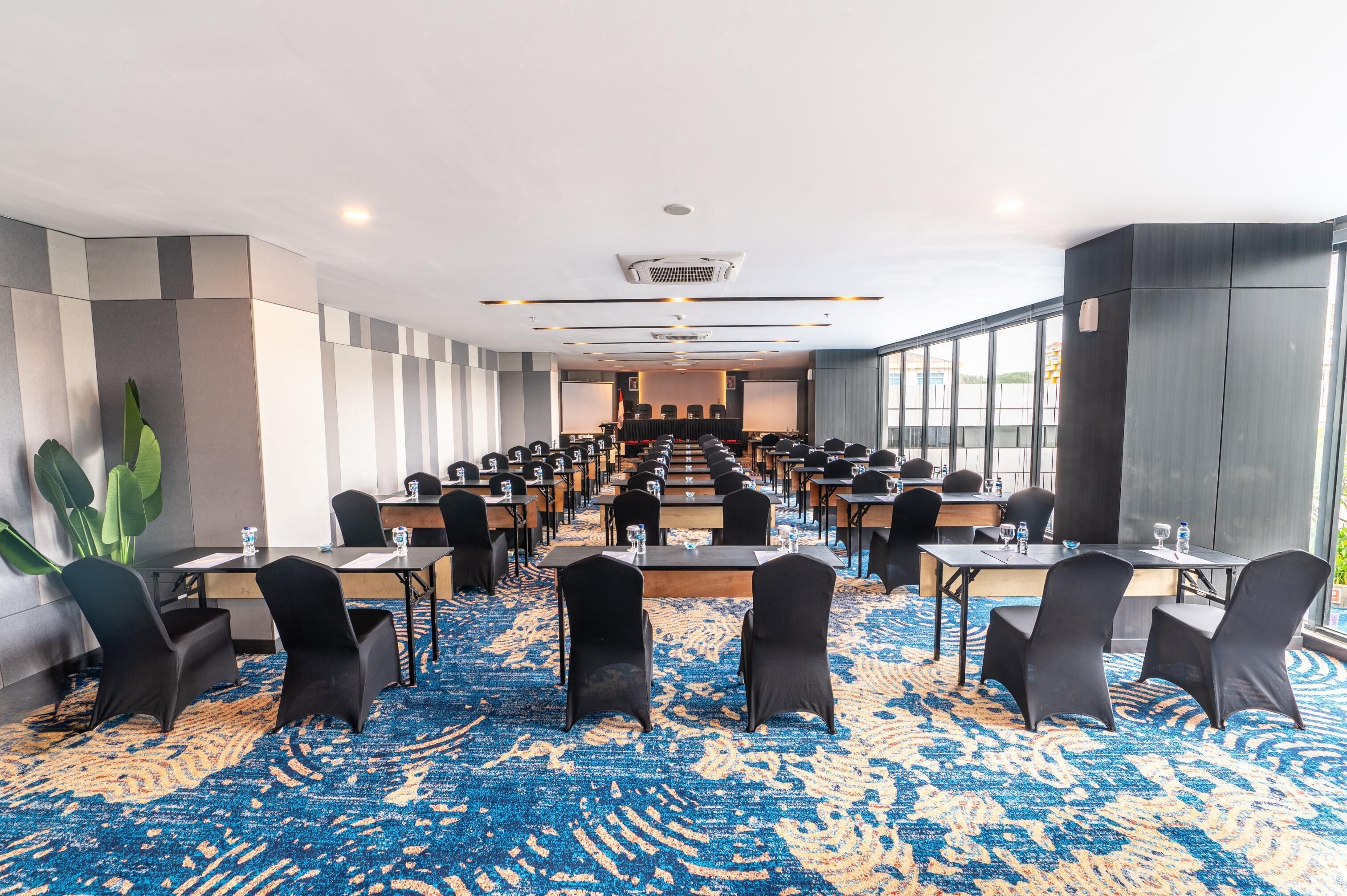 A conference room with multiple tables and chairs, large windows, and a patterned carpet.
