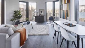 En moderne stue med en hvid sofa, et spisebord med stole, et stort vindue med byudsigt og en balkon med udsigt over byen.
