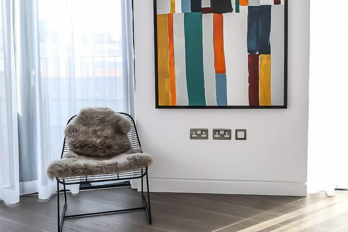 A modern room with a large abstract painting, a fluffy chair, and a view through sheer curtains.