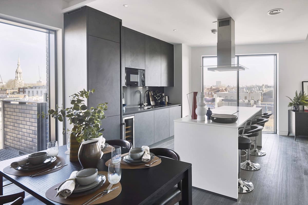 A modern kitchen with dark cabinetry, a central island with bar stools, and a large window offering a city view.
