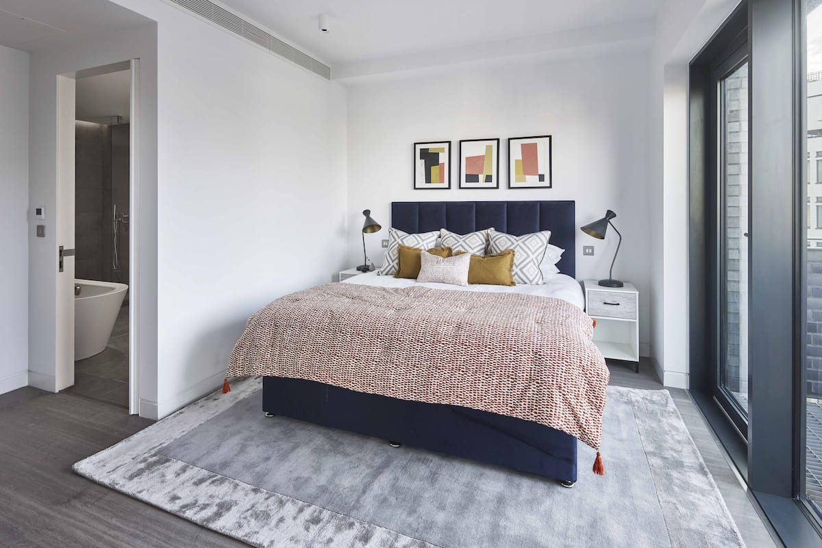 A modern bedroom with a large bed, bedside tables, a nightstand, and a view through a large window.