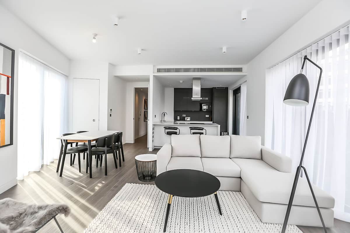 A modern living room with a sofa, a dining table, and a kitchen in the background.