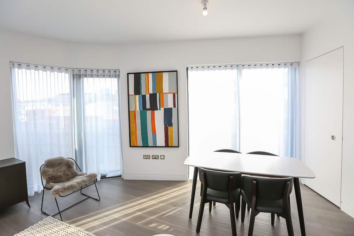 A modern, well-lit room with a dining table, chairs, a fluffy chair, and a large abstract painting on the wall.