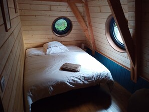 Cozy cabin with a sloped ceiling and exposed wooden beams, featuring a comfortable bed and two windows.