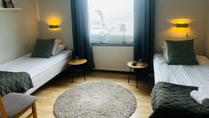 A hotel room with two single beds, a small round table, a chair, a round rug, and a window with curtains.