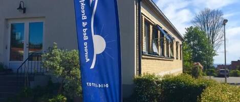 A building with a blue flag featuring a white bird and text, a stone bench, and a well-maintained garden.