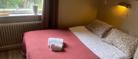 Ein Hotelzimmer mit Bett, einem Vorhangfenster, einem Heizkörper, einer Lampe und einer Pflanze.