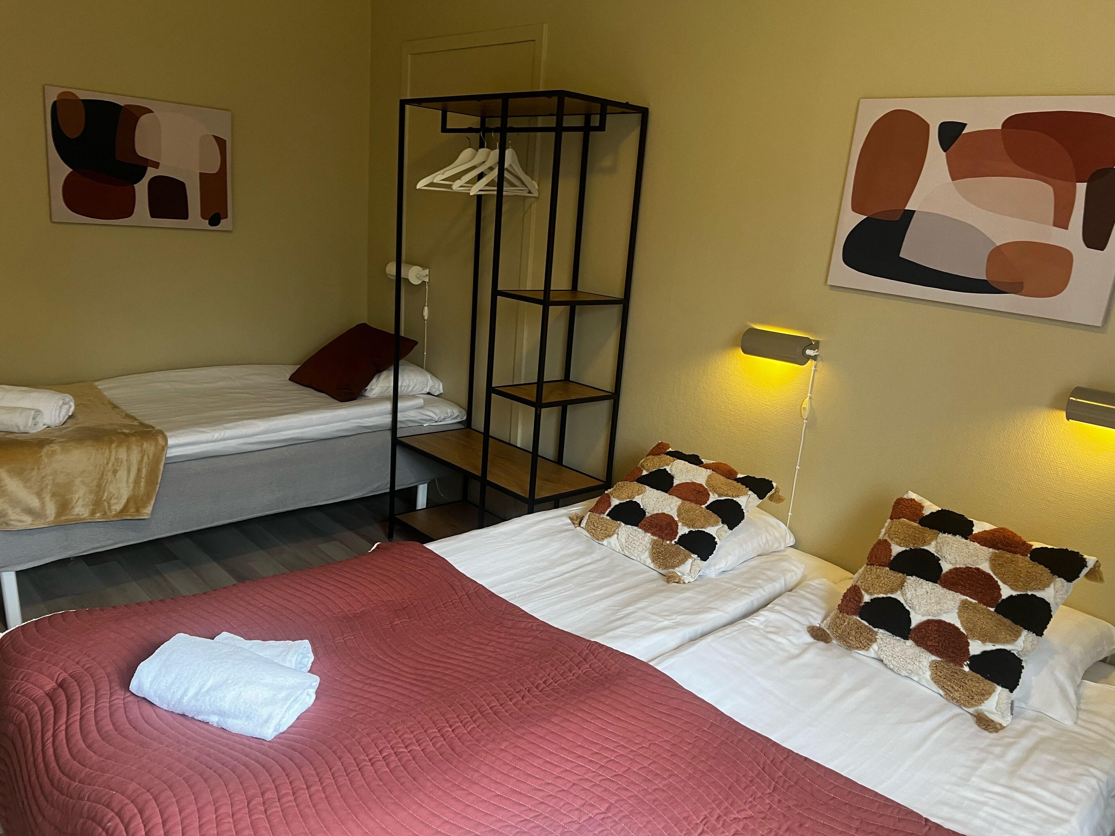 Een hotelkamer met twee bedden, een kledingkast, abstracte wanddecoratie en een bedlampje.
