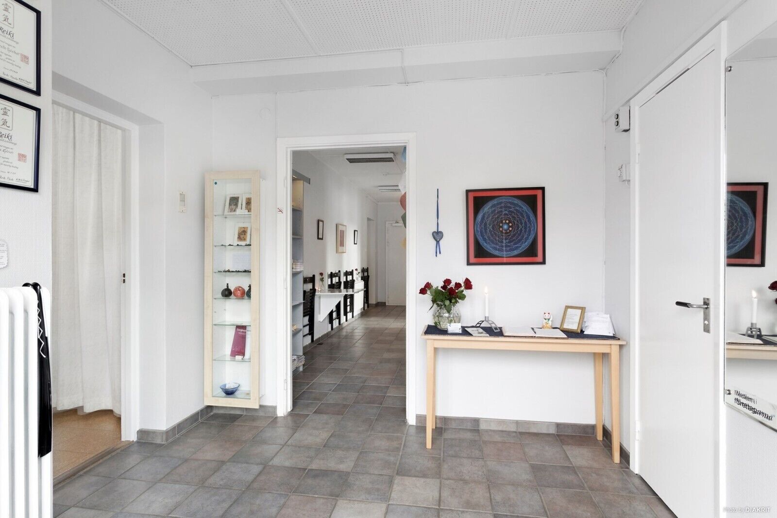 A hallway with a reception desk, framed artwork, and a door leading to another room.