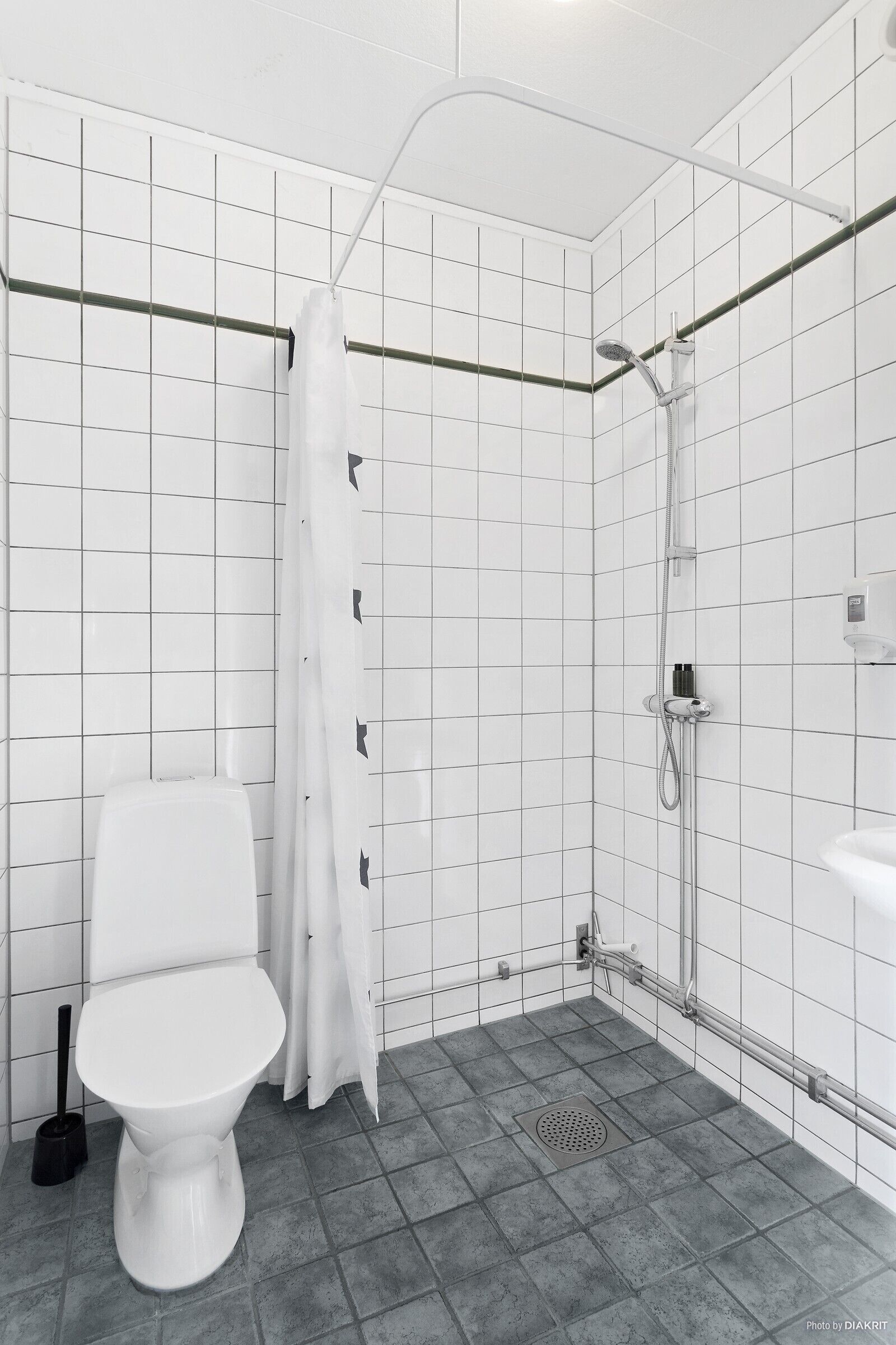 Une salle de bain avec des toilettes blanches, une douche dotée d’une porte en verre et un sol carrelé.