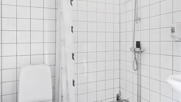 Une salle de bain avec des toilettes blanches, une douche dotée d’une porte en verre et un sol carrelé.