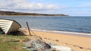 A boat on a sandy beach with a calm sea and a cloudy sky.