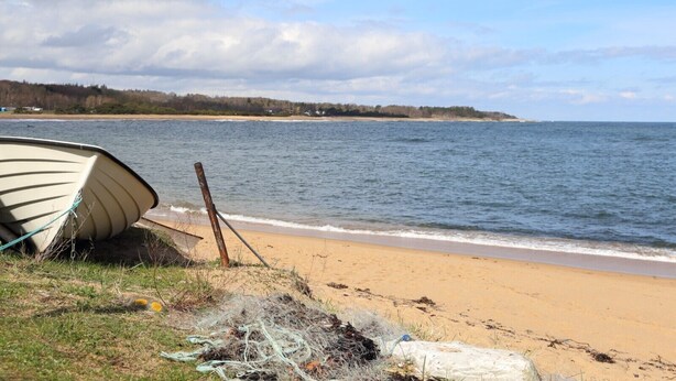 A boat on a sandy beach with a calm sea and a cloudy sky.