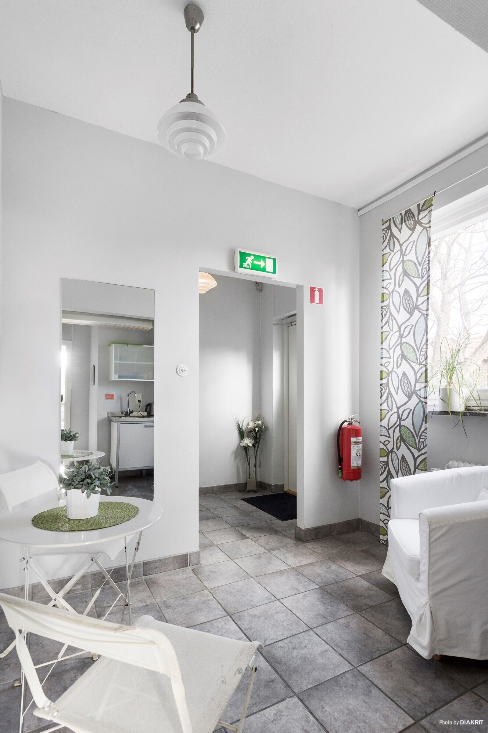 A modern hotel lobby with a reception desk, a seating area, a kitchenette, and a fire extinguisher.