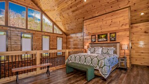 Un dormitorio tipo cabaña de madera con una cama grande, techo de madera y un balcón con baranda de madera.