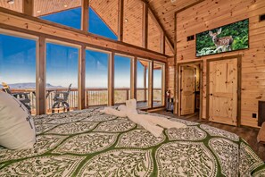 Relax in a spacious room with a large bed, high ceiling, and large windows offering a view of the outdoors.