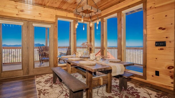 Interior de madera con una gran mesa de comedor, bancos y vistas a la montaña a través de amplias ventanas.