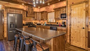 Una cocina al estilo de cabaña de madera con una isla central, taburetes de bar y electrodomésticos integrados.